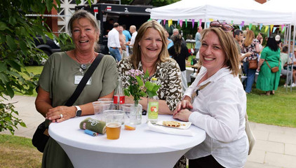 Drei Mitarbeiterinnen stehen an einem mit weißem Stoff bezogenen Stehtisch mit Blumenschmuck und Getränken und lächeln in die Kamera beim Sommerfest 2026 auf dem Gesundheitscampus Volksdorf des Evangelischen Amalie Sieveking Krankenhauses, der Residenz am Wiesenkamp, des Feierabendhauses Volksdorf und der Albertinen Kindertagesstätte Volksdorf. Drei Mitarbeiterinnen stehen an einem mit weißem Stoff bezogenen Stehtisch mit Blumenschmuck und Getränken und lächeln in die Kamera beim Sommerfest 2026 auf dem Gesundheitscampus Volksdorf des Evangelischen Amalie Sieveking Krankenhauses, der Residenz am Wiesenkamp, des Feierabendhauses Volksdorf und der Albertinen Kindertagesstätte Volksdorf.