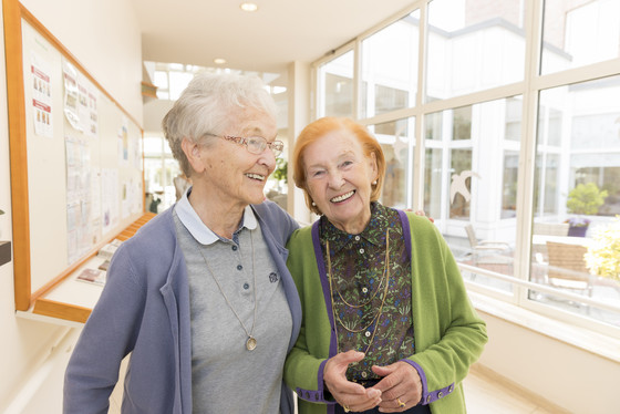 Zwei Seniorinnen schlendern lachend durch einen Flur, enthaltene Leistungen im Wohngeld, Unterstützung im Alltag im Seniorenheim, Angebot in der Residenz am Wiesenkamp, Hamburg-Volksdorf
