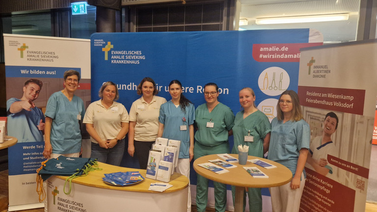 Sieben Mitarbeiterinnen der Hamburger Einrichtungen der Immanujel Albertinen Diakonie stehen nebeneinander an einem Stand auf der Berufsorientierungsmesse Sieben Mitarbeiterinnen der Hamburger Einrichtungen der Immanujel Albertinen Diakonie stehen nebeneinander an einem Stand auf der Berufsorientierungsmesse