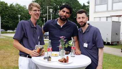 Drei Mitarbeiter stehen in Funktionskleidung an einem Stehtisch mit Blumenschmuck und Getränken und blicken in die Kamera beim Sommerfest 2026 auf dem Gesundheitscampus Volksdorf des Evangelischen Amalie Sieveking Krankenhauses, der Residenz am Wiesenkamp, des Feierabendhauses Volksdorf und der Albertinen Kindertagesstätte Volksdorf. Drei Mitarbeiter stehen in Funktionskleidung an einem Stehtisch mit Blumenschmuck und Getränken und blicken in die Kamera beim Sommerfest 2026 auf dem Gesundheitscampus Volksdorf des Evangelischen Amalie Sieveking Krankenhauses, der Residenz am Wiesenkamp, des Feierabendhauses Volksdorf und der Albertinen Kindertagesstätte Volksdorf.