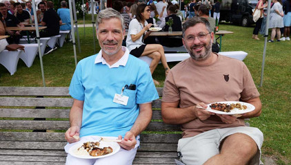 Zwei Mitarbeiter sitzen mit vollen Tellern auf einer Sitzank und blicken in die Kamera beim Sommerfest 2026 auf dem Gesundheitscampus Volksdorf vom Evangelischen Amalie Sieveking Krankenhaus, Residenz am Wiesenkamp, Feierabendhaus Volksdorf und Albertinen Kindertagesstätte Volksdorf. Zwei Mitarbeiter sitzen mit vollen Tellern auf einer Sitzank und blicken in die Kamera beim Sommerfest 2026 auf dem Gesundheitscampus Volksdorf vom Evangelischen Amalie Sieveking Krankenhaus, Residenz am Wiesenkamp, Feierabendhaus Volksdorf und Albertinen Kindertagesstätte Volksdorf.