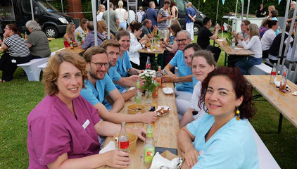 Mehrere Mitarbeitende sitzen in Funktionskleidung an einer mit Blumen geschmückten Bierbank mit Essensschalen und Getränken beim Sommerfest 2026 auf dem Gesundheitscampus Volksdorf des Evangelischen Amalie Sieveking Krankenhauses, der Residenz am Wiesenkamp, des Feierabendhauses Volksdorf und der Albertinen Kindertagesstätte Volksdorf. Mehrere Mitarbeitende sitzen in Funktionskleidung an einer mit Blumen geschmückten Bierbank mit Essensschalen und Getränken beim Sommerfest 2026 auf dem Gesundheitscampus Volksdorf des Evangelischen Amalie Sieveking Krankenhauses, der Residenz am Wiesenkamp, des Feierabendhauses Volksdorf und der Albertinen Kindertagesstätte Volksdorf.