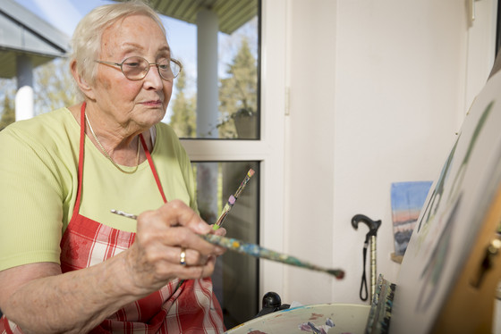 Eine Seniorin steht malend an einer Staffelei, Unterstützung und Hilfe im Alltag im Seniorenheim, Therapieangebot in der Seniorenresidenz, Hamburg-Volksdorf 